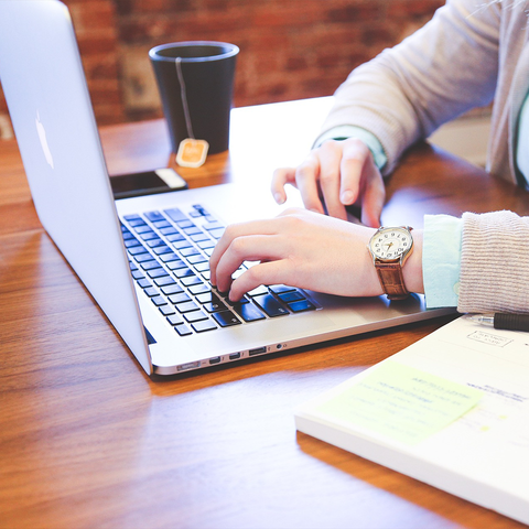 A customer working on a laptop, with a cup of tea and a notebook on the desk